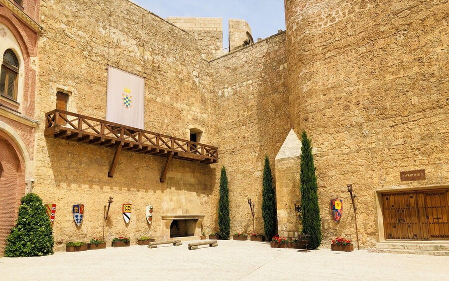 A courtyard with stone walls, wooden beams, and flags. 2