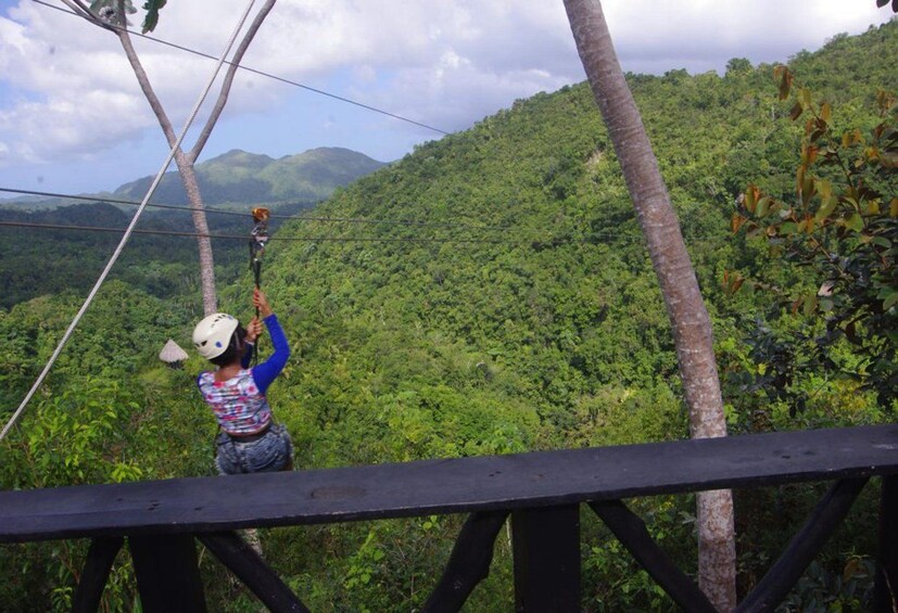 En person suser ned gennem luften på en zipline over en frodig, grøn skov med et bjerg i baggrunden. 4