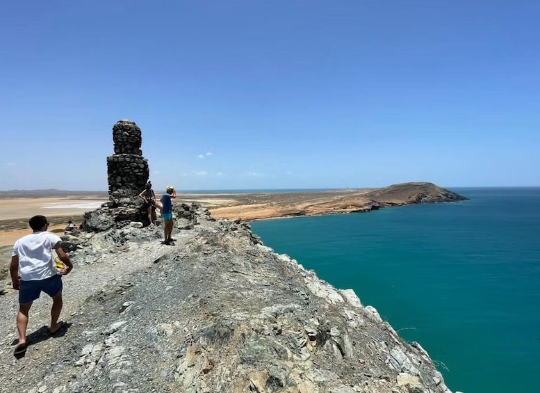 A rocky coastline with a clear blue sea, a small island, and a stone structure. 5