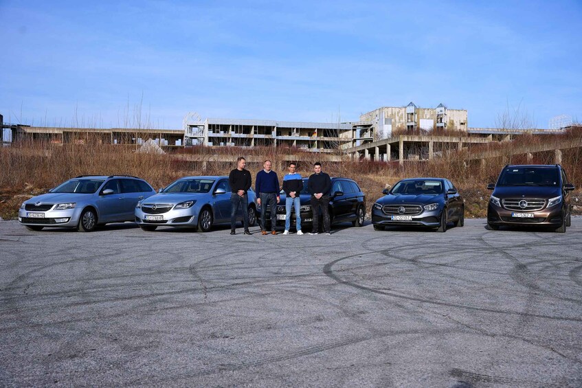 A group of people standing in front of a row of cars with a building under construction in the background. 3