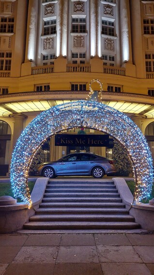 A car parked under a decorative archway with lights, in front of a building with classical architecture. 5