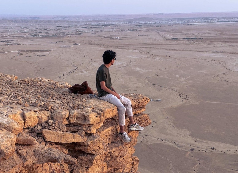 Una persona sentada sobre un promontorio rocoso con vistas a un extenso paisaje desértico. 1