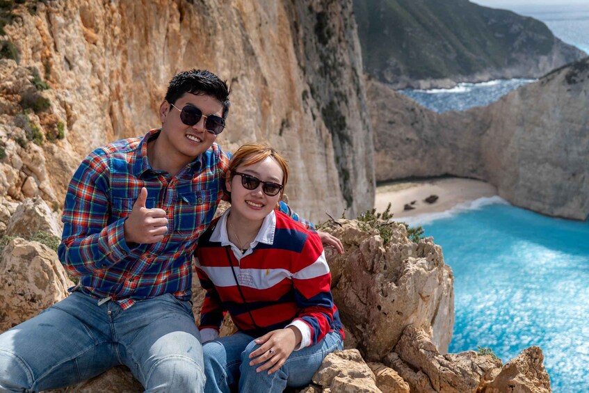 Un couple est assis sur une falaise rocheuse, d’où l’on a une vue sur une zone côtière avec des falaises et une plage. 3
