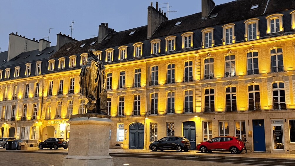 Un edificio histórico con ventanas iluminadas y una estatua al frente. 2