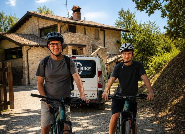 To personer på cykel foran en bygning i sten med en parkeret varevogn. 3