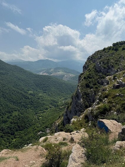 A mountainous landscape with dense green forests, rocky outcrops, and a winding road in the distance. 4
