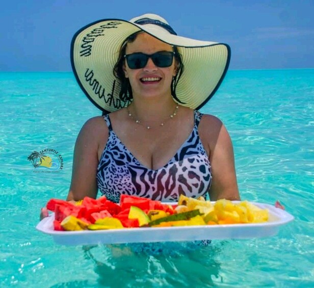 Una persona en traje de baño sosteniendo una bandeja con fruta en agua cristalina azul. 3