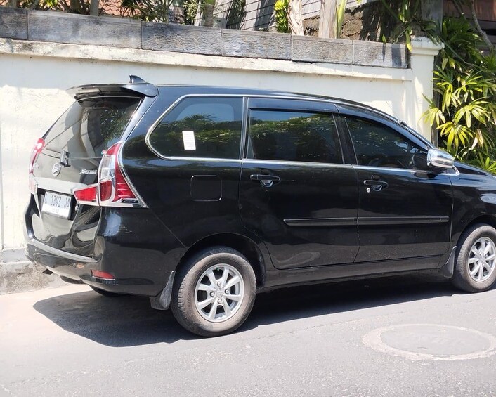 Une voiture noire à hayon, garée dans une rue, avec un mur blanc et quelques plantes en arrière-plan. 5