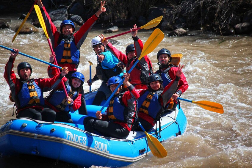 A group of people in a blue inflatable raft with paddles, navigating a river. 1