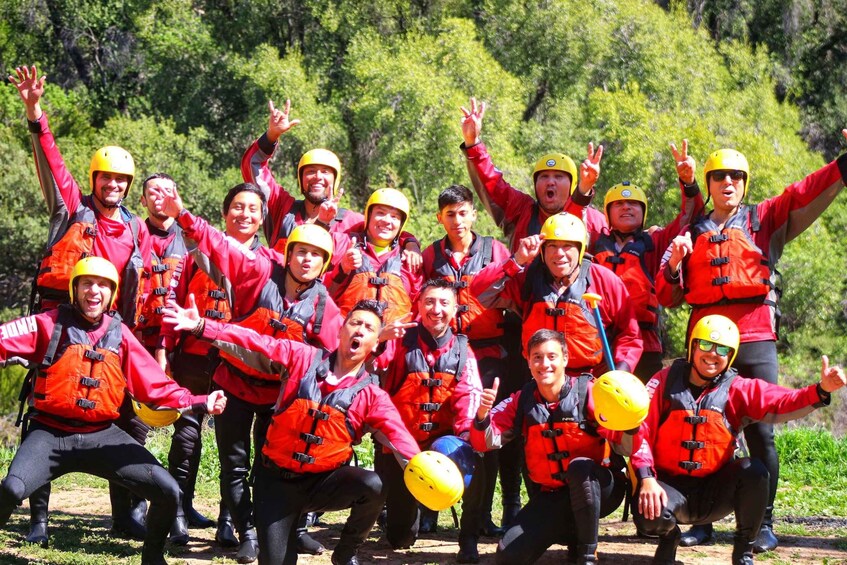 A group of people in red jackets and yellow helmets posing for a photo in a forested area. 5