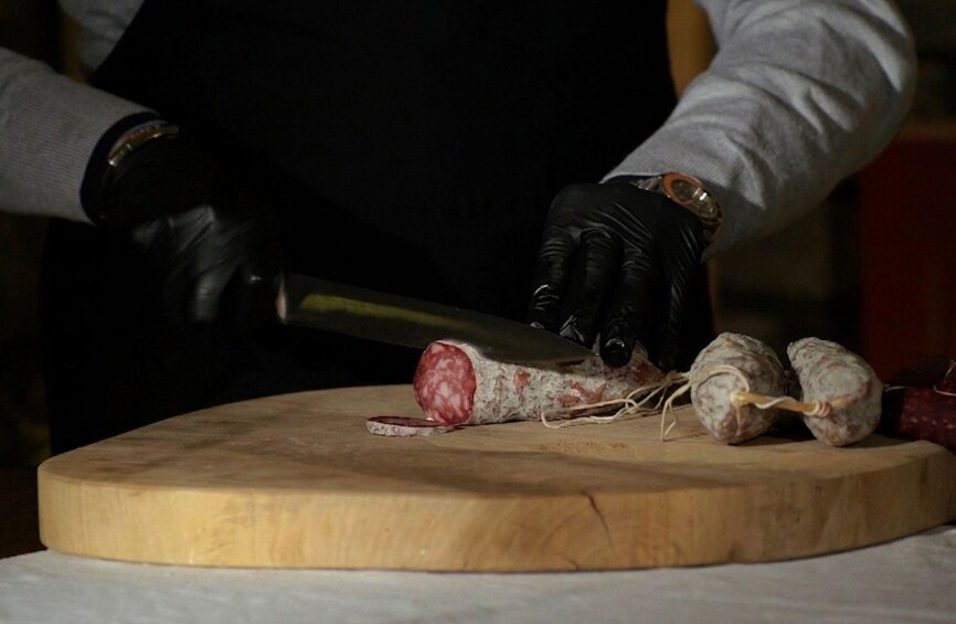 A person slicing a large piece of cured meat on a wooden cutting board. 5