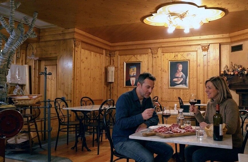 A wooden interior with tables and chairs, a chandelier, and paintings on the walls. 1