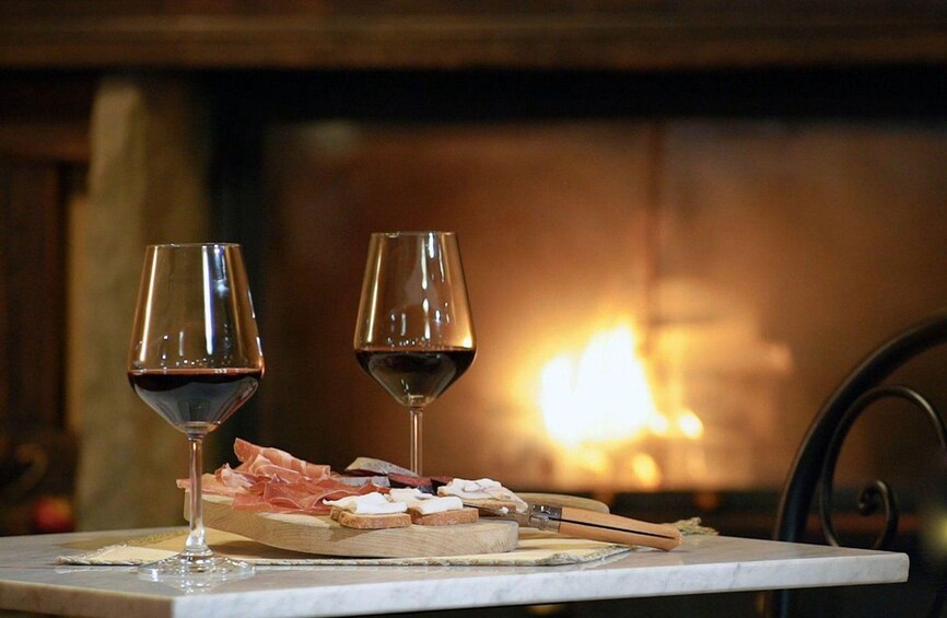 Two wine glasses on a table with a charcuterie board and a fireplace in the background. 3