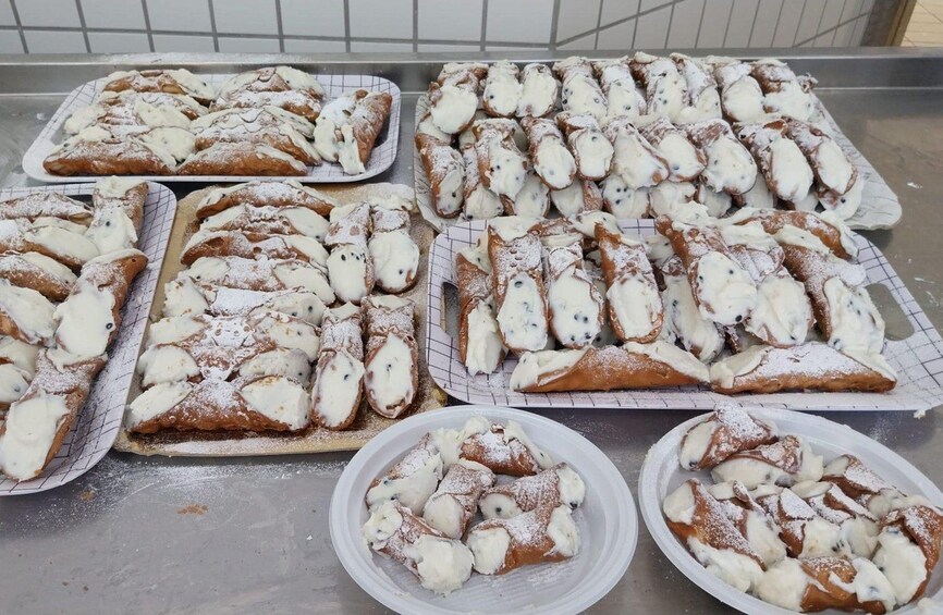 Trays of cannoli with white cream filling and powdered sugar. 4