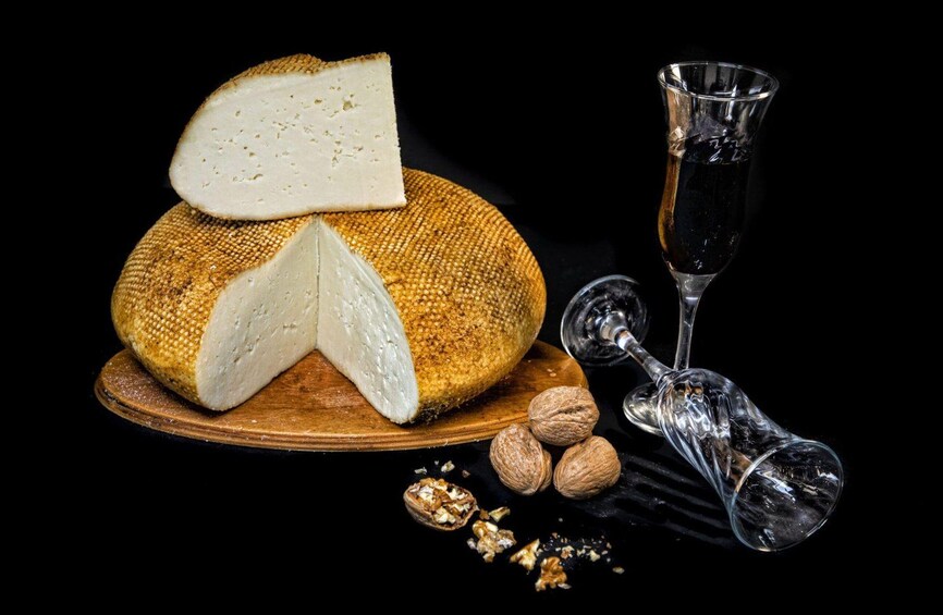 A wheel of cheese, a glass of wine, and walnuts on a wooden board. 1