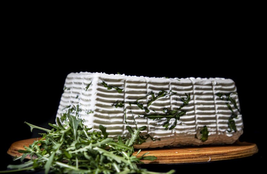 A wheel of cheese with green herbs on top, placed on a wooden board. 2