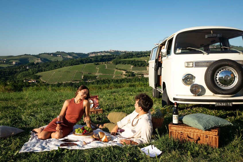 A picnic on a grassy hill with a vintage car parked nearby. 1