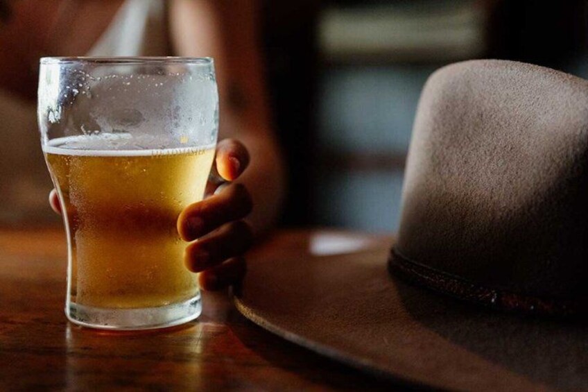 A glass of beer on a wooden table with a hat beside it. 5