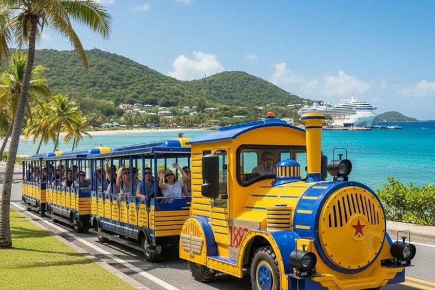 A yellow and blue train with passengers, a beach, a cruise ship, and palm trees. 2