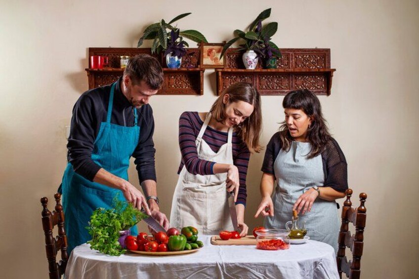 Three people preparing food with vegetables and a cutting board on a table. 4