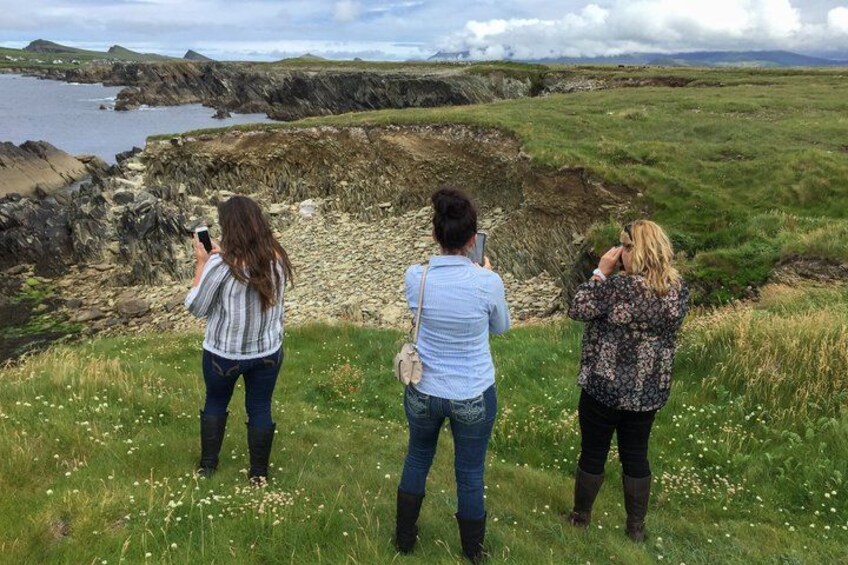 Three people taking photos of a coastal landscape with cliffs and grassy fields. 4