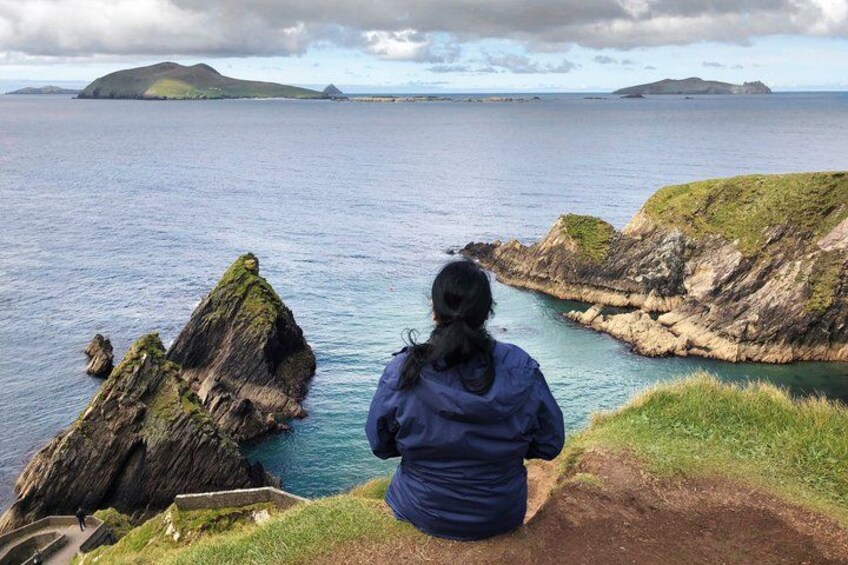 A person sitting on a cliff overlooking a coastal landscape with rocky outcrops and calm sea. 1