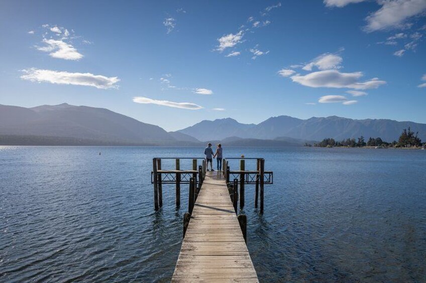 A wooden pier extending into a calm lake with mountains in the background. 1