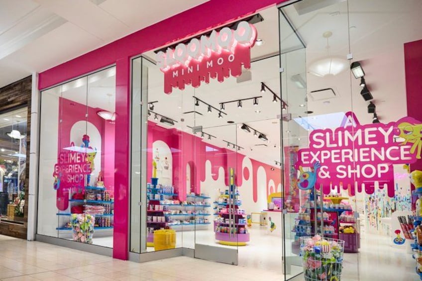A brightly lit store with a pink and white color scheme, featuring a sign that reads 'SLIMEY EXPERIENCE & SHOP.' 5