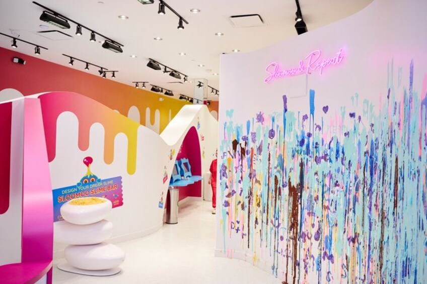 A colorful interior with a neon sign, a white bench, and a wall with a drip paint design. 1