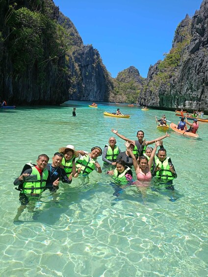 A group of people kayaking in a clear, turquoise sea surrounded by rocky cliffs. 1
