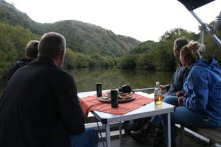 A group of people sitting at a table with a meal, overlooking a lake and hills. 4