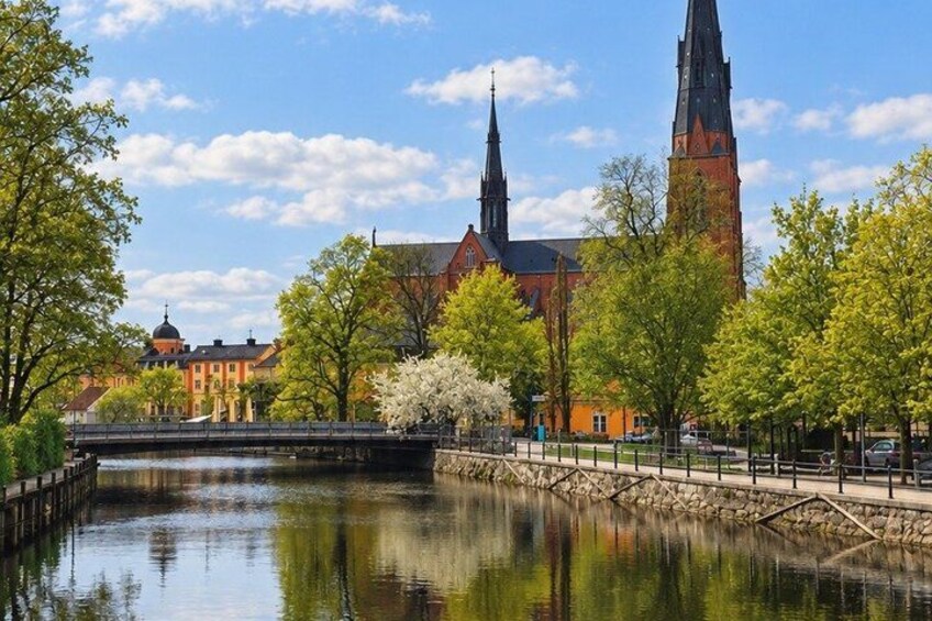A river with a bridge, a church with a tall spire, and trees with green leaves. 4