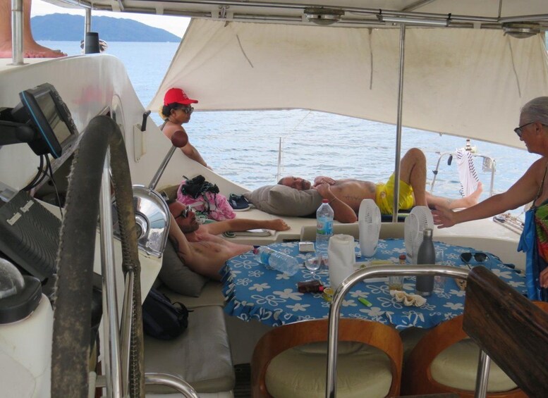A boat with a covered area, a table with a blue floral tablecloth, and people relaxing on the deck. 2