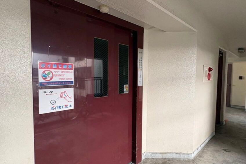 A hallway with a red door, a sign with Japanese text, and a fire alarm button. 4