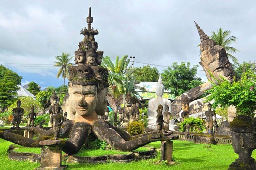 A large Buddha statue surrounded by smaller statues in a lush garden. 1