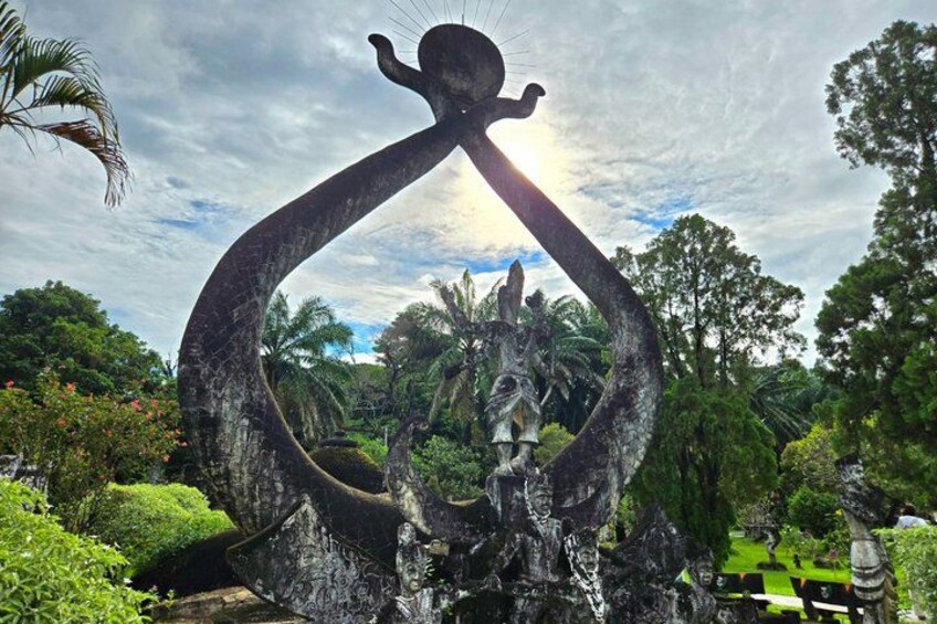 A large sculpture of a figure holding a ring, surrounded by lush greenery and trees. 4