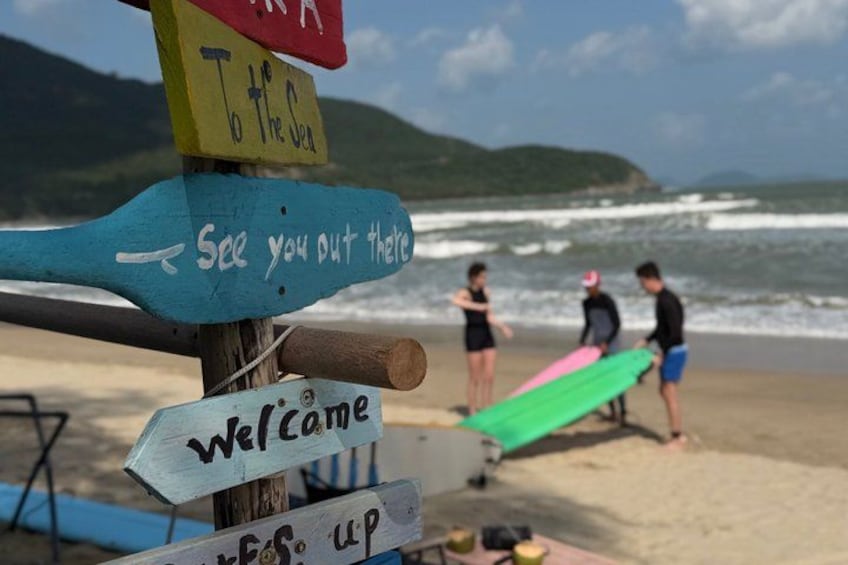 A beach with a wooden signpost with multiple directional signs, a green surfboard, and people on the sand. 5