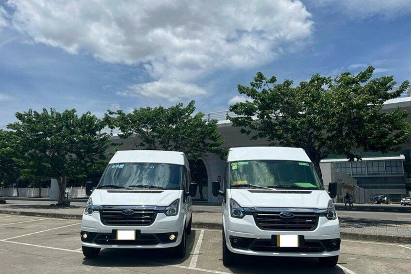 Two white vans parked in a parking lot with trees and a building in the background. 1