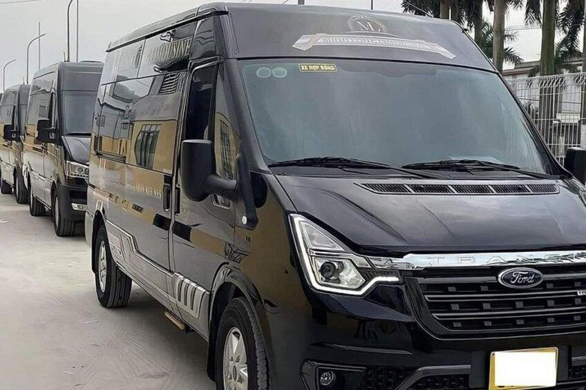 A black Ford Transit van with a reflective surface, parked on a concrete surface with other similar vehicles in the background. 4
