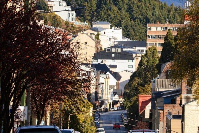 A street lined with cars and buildings, trees with autumn leaves, and a hilly background. 4