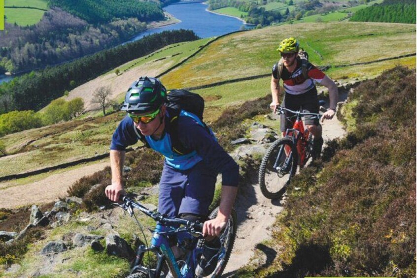 Two cyclists on a mountain trail with a river in the background. 2