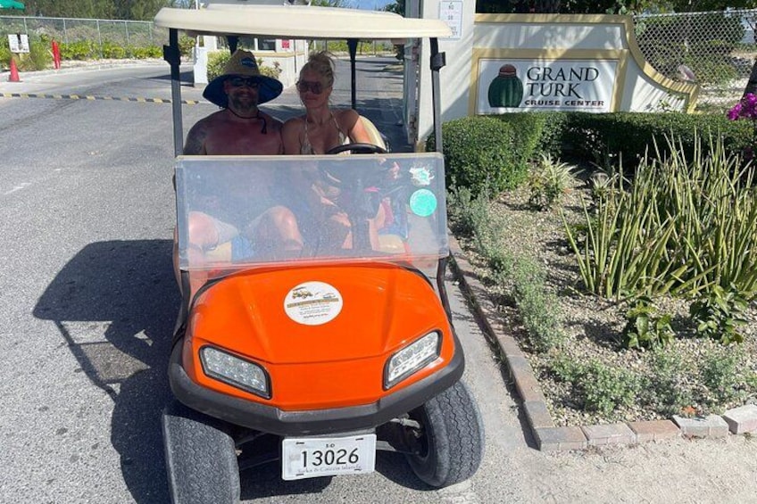 A golf cart with a sticker, parked near a sign for Grand Turk Cruise Center. 3