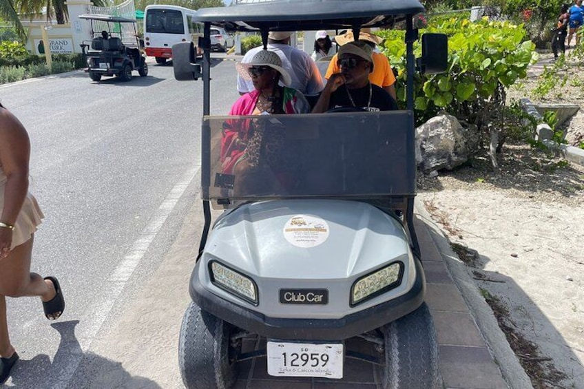 A golf cart with a license plate, parked on a road with people around. 4