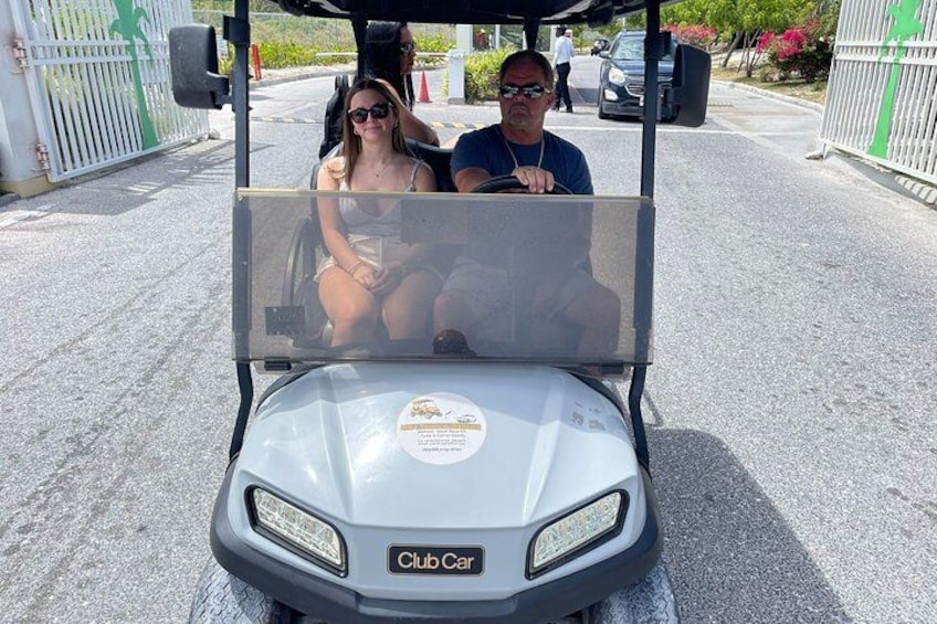 A golf cart with a Club Cart sticker, a person driving, and a woman sitting in the back. 5
