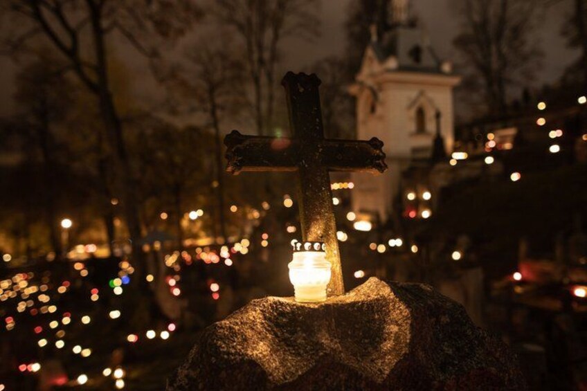 A cross with a candle, surrounded by blurred lights in a nighttime setting. 2
