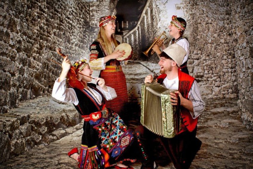 A group of people in traditional attire playing musical instruments in a stone-walled setting. 2