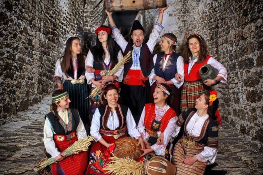 A group of people in traditional attire, standing in front of a stone wall. 3