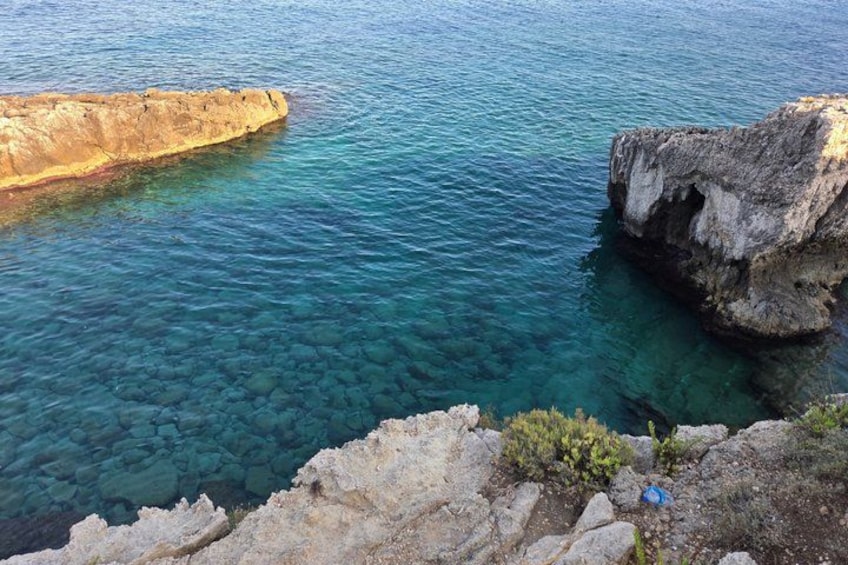 A coastal landscape with clear blue water, rocky formations, and a cliff edge. 4