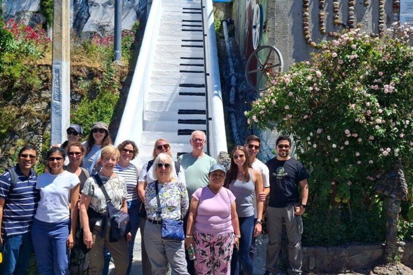 A group of people standing in front of a piano-like structure with a staircase leading up to it. 4