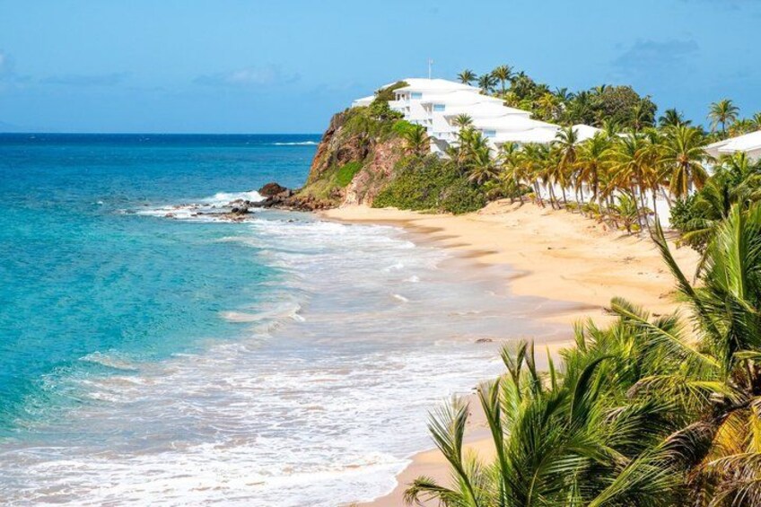 A beach with clear blue water, sandy shore, and a white building on a cliff. 5